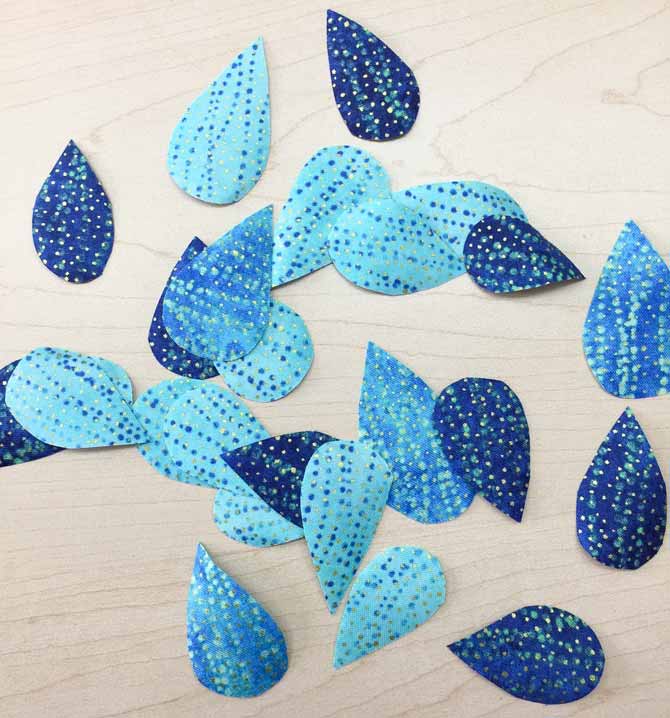 An assortment of fabric raindrop shapes with fusing on the back in 3 different hues of blue. Northcott’s Artisan Spirit Shimmer Echoes.