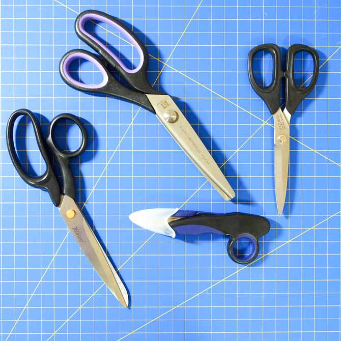 4 pairs of scissors in varying sizes with black handles and silver blades on a blue cutting mat
