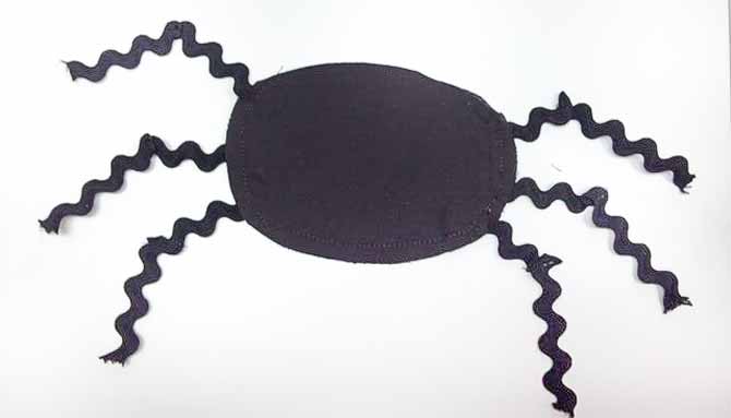 Black fabric spider with bent legs out of rick rack on table.