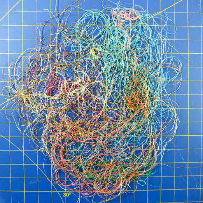 A variety of thread ends that look like a bird's nest sitting on a blue mat