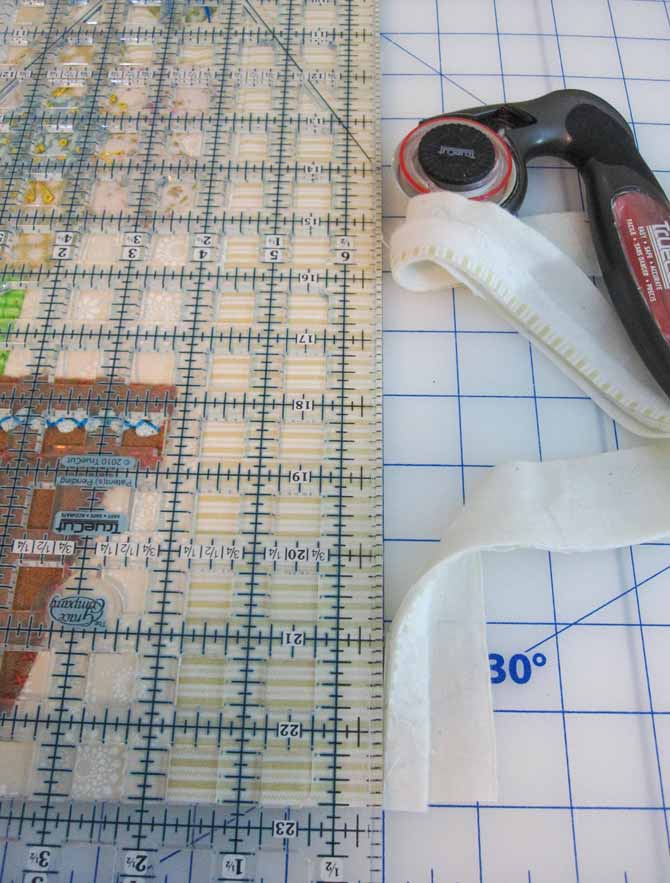 A quilter's ruler and rotary cutter set on a cutting board to trim the studio bird mini quilt. WonderFil Specialty Threads.